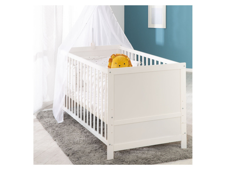 Een witte babywieg met een hemel en een knuffeldier in de vorm van een leeuw.