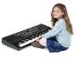 Een jong meisje zit op de grond en speelt op een zwart elektronisch keyboard.