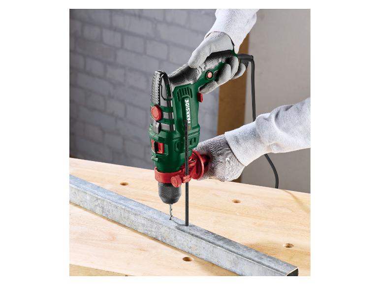 Klopboormachine in handen, boort in een metalen profiel op een houten tafel.