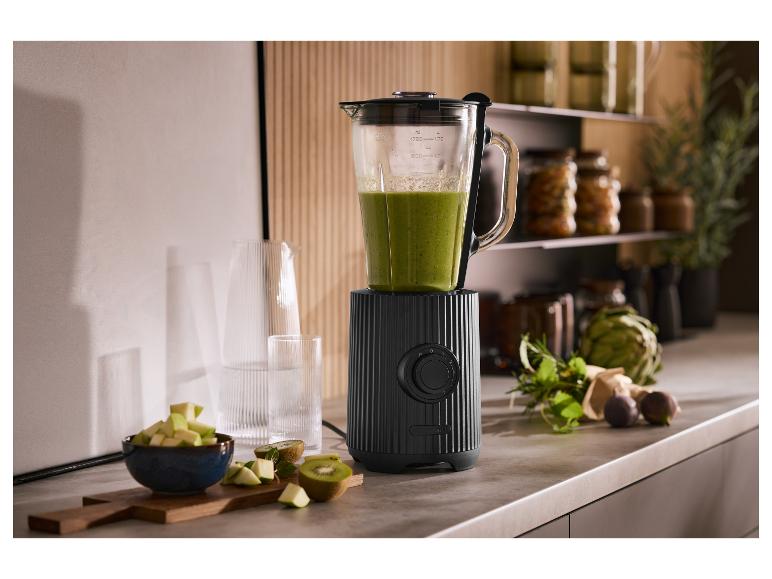 Zwarte blender met groene smoothie, fruit en kruiden in de keuken.