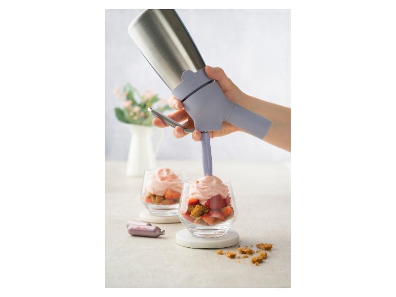 Een hand gebruikt een slagroomdispenser om roze mousse toe te voegen aan een aardbeidessert.