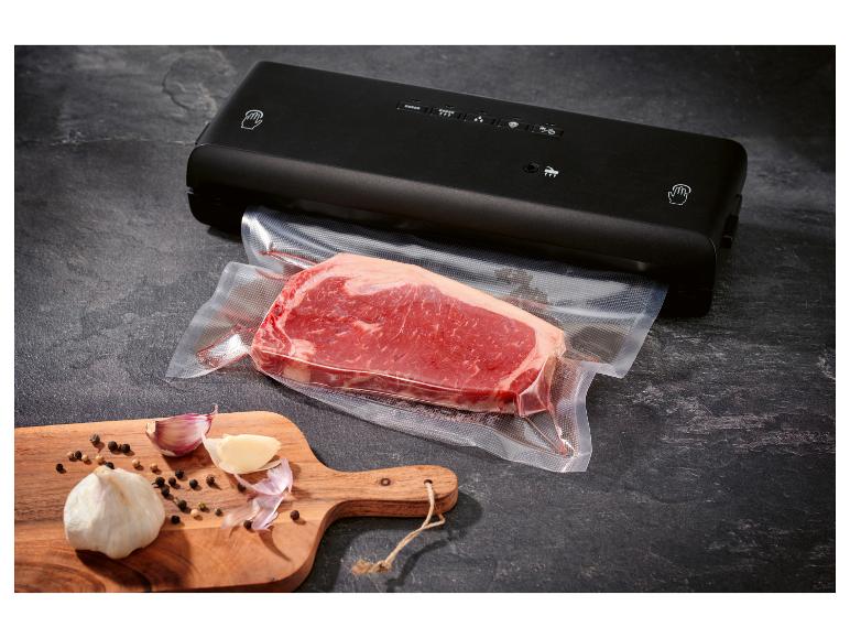 Zwarte vacuümmachine met een vacuüm verpakt stuk rundvlees en knoflook op een snijplank.