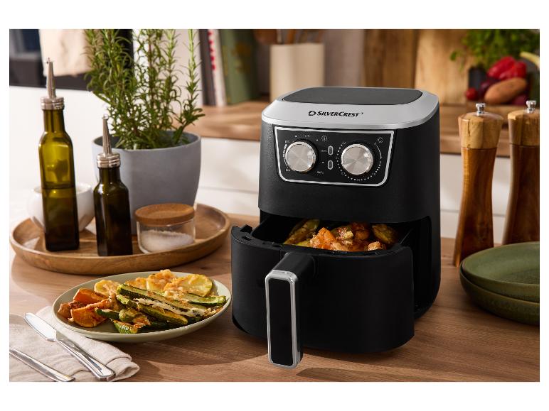 SILVERCREST airfryer met gekookte groenten, olieflesjes en kruiden op een houten tafel.