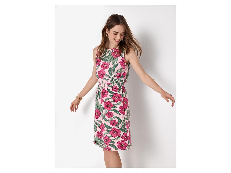 Vrouw in een roze bloemen zomerjurk met groene bladeren, lachend en naar beneden kijkend.