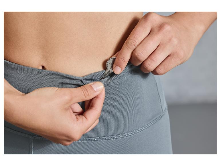 Een vrouw stopt een sleutel in de zak van een grijze legging.