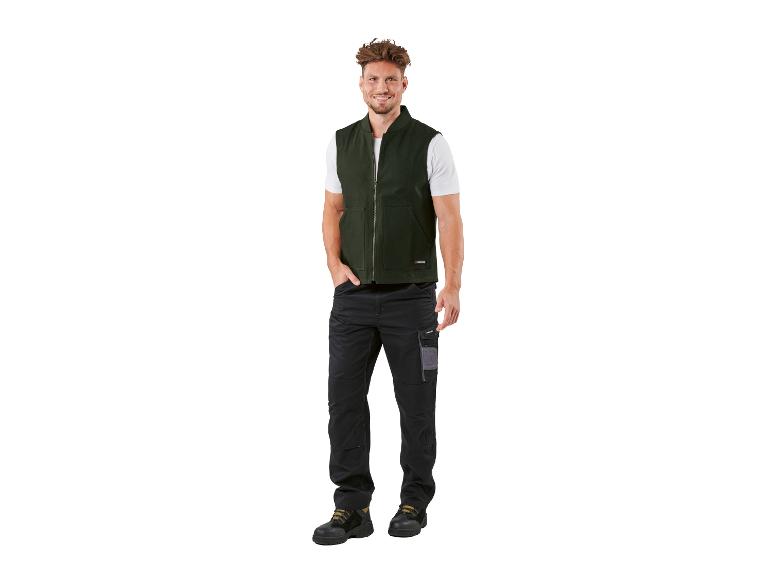 Lachende man draagt donkergroen vest, wit T-shirt en zwarte werkbroek.
