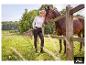 Vrouw in ESMARA® slim fit broek staat bij een hek met een paard. [AI-gegenereerde afbeelding]