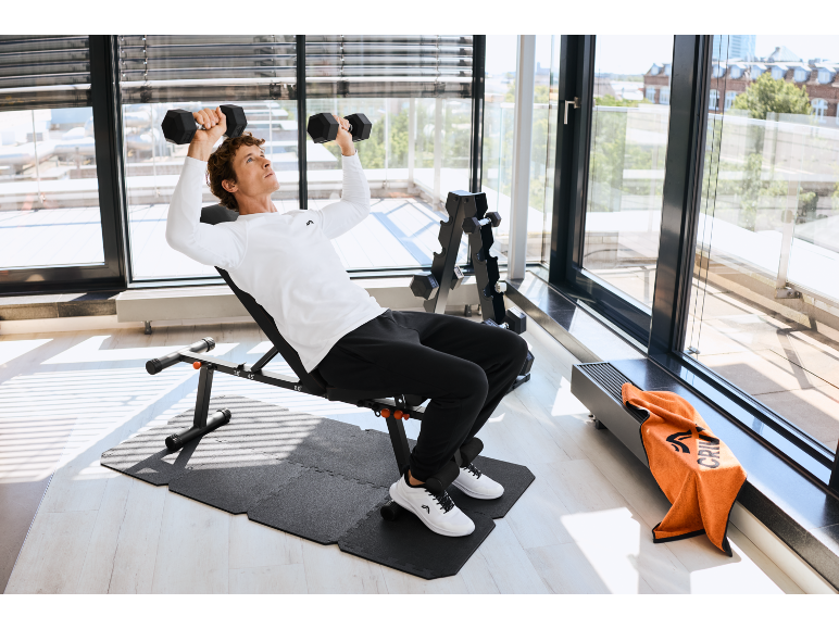 Man tilt halters op een verstelbare halterbank in een thuisgym met halterrek.