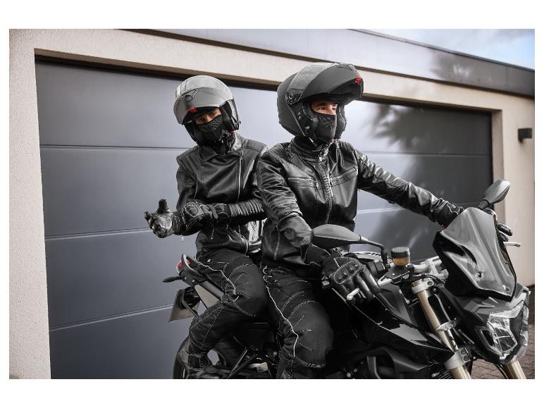 Twee motorrijders met helmen en leren jassen op een motor voor een garage