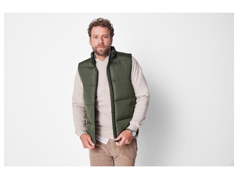 Een man in een groene gewatteerde vest en een beige trui.