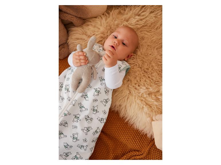 Een baby in een Winnie de Poeh slaapzak met een knuffelbeer