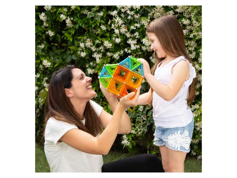 Lachende moeder en dochter spelen met kleurrijke magnetische bouwblokken in de tuin.