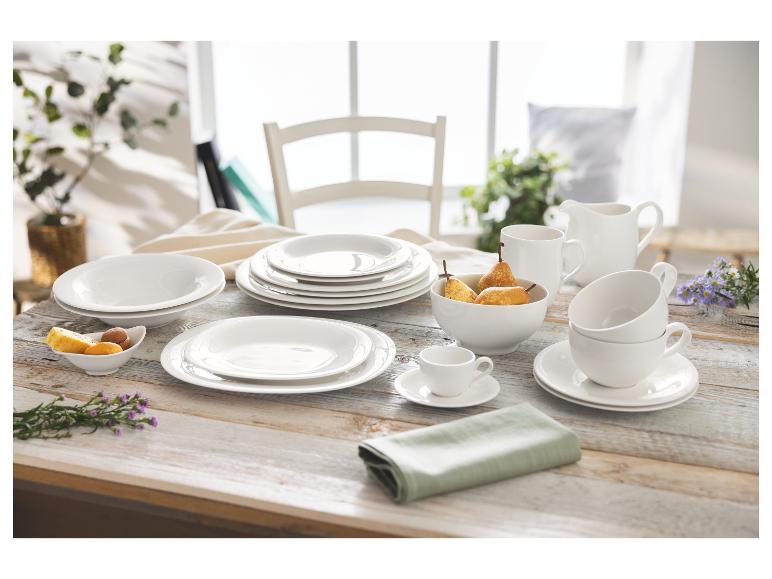 Wit porseleinen servies op een rustieke houten tafel, met fruit en bloemen.