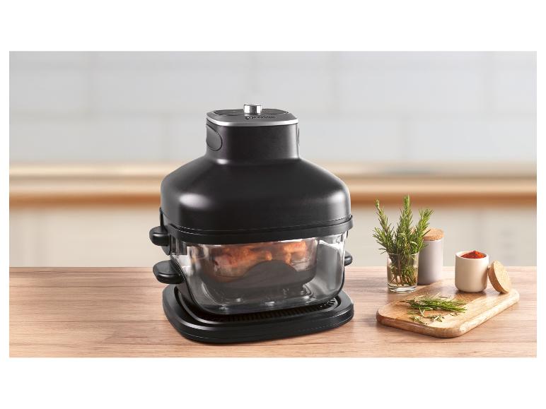 Zwarte airfryer met eten erin, op een houten tafel met kruiden en specerijen.