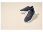 Twee blauwe suède sneakers met witte zolen, geplaatst op een beige standaard.