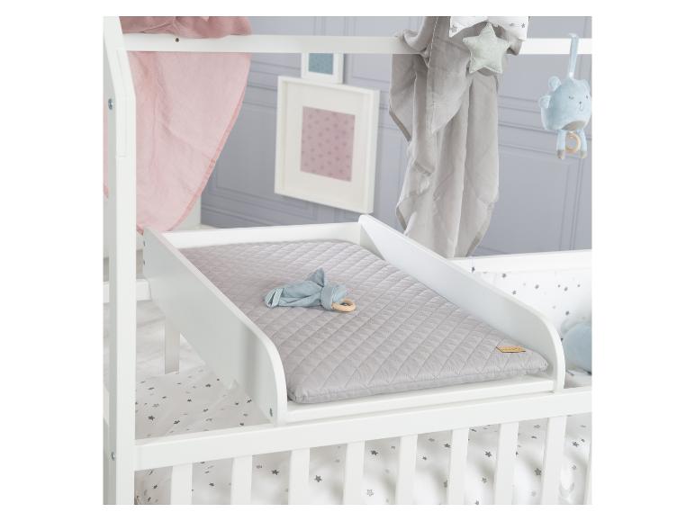 Witte commode met een grijs aankleedkussen, geplaatst boven een babybedje.