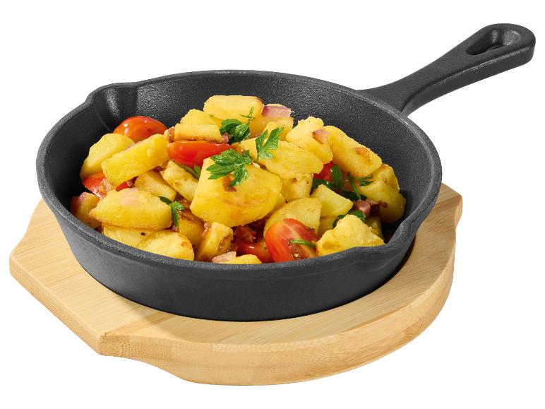Gebakken aardappelen met tomaten, uien en peterselie in een gietijzeren pan op een houten onderzetter.