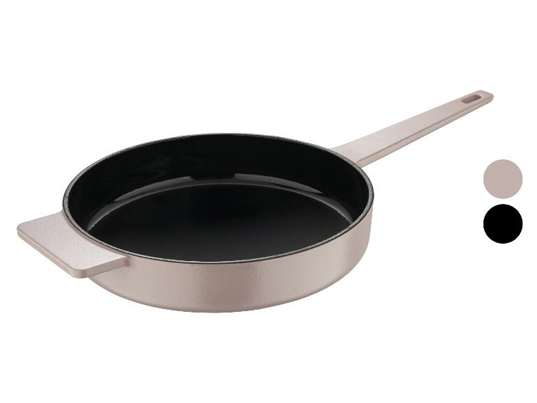 Beige gietijzeren pan met zwarte binnenkant en twee kleurstaaltjes.