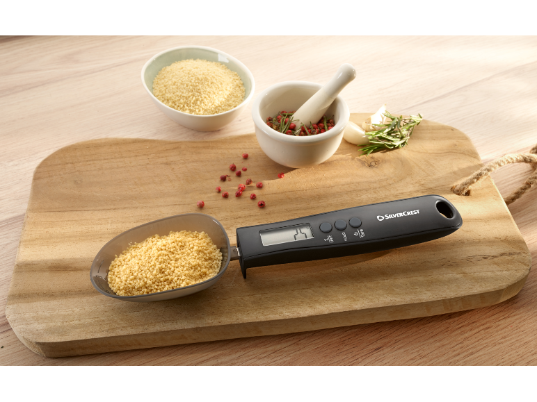Digitale maatlepel met couscous op een houten plank met kruiden