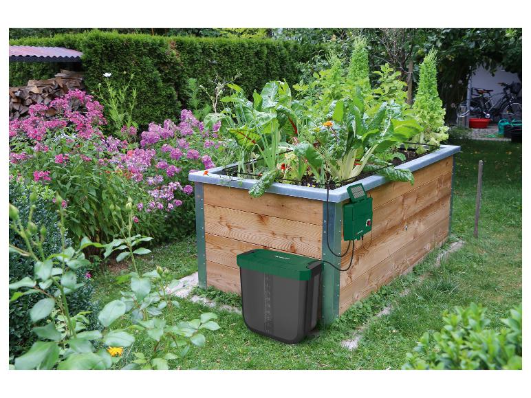 Irrigatiesysteem met tank en zonnepaneel in een houten verhoogde moestuin met groenten en bloemen.
