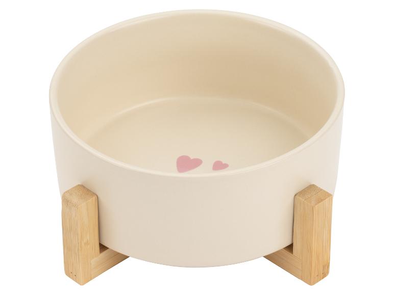 Crèmekleurige keramische voerbak voor huisdieren op een houten standaard, versierd met roze hartjes.
