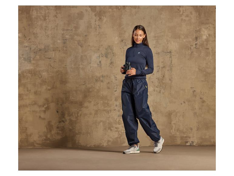 Een vrouw draagt blauwe regenbroek en een donkerblauwe trui met een capuchon.