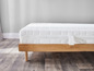 Een wit matras op een houten bedframe op een houten vloer.