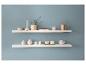 Twee witte planken met diverse decoratieve items zoals vazen, kaarsen en een gouden gieter tegen een blauwe muur.