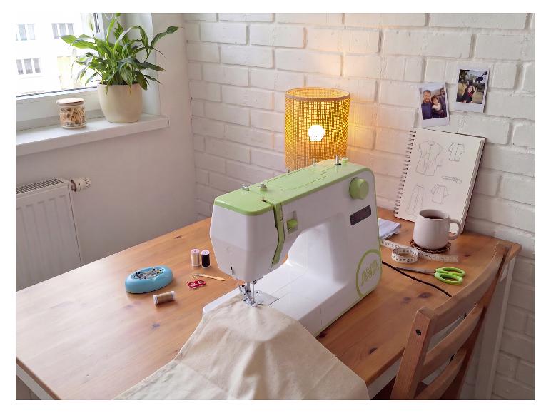Naaimachine op een houten bureau met naaibenodigdheden, een plant en een lamp.