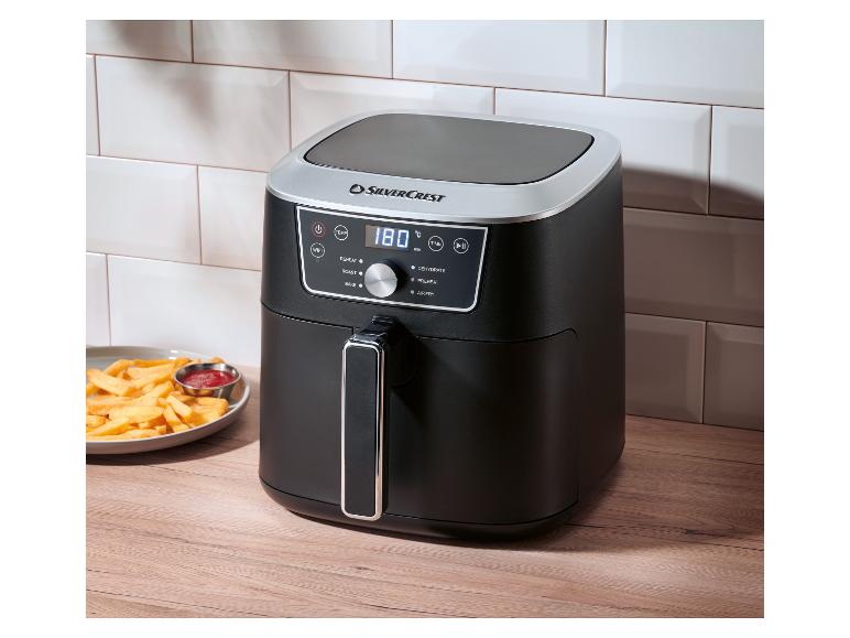 Een zwarte en zilveren airfryer met een digitaal display dat 180 graden Celsius aangeeft, naast een bord friet en ketchup.