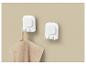 Twee witte wandhaken, één met een beige handdoek, tegen een lichtbruine muur.