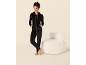 Vrouw in zwart velours trainingspak met capuchon en broek, staand naast een witte fauteuil.