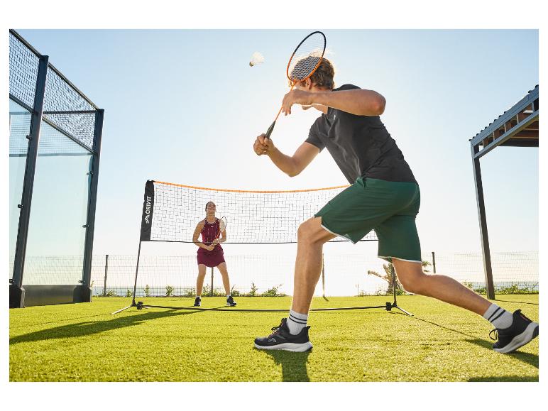 Twee mensen spelen badminton buiten op een groen gazon met een net.