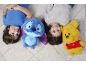 Twee lachende kinderen liggen op een tapijt met twee knuffels, een blauwe en een gele.