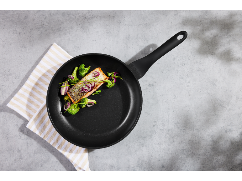 Zalm en broccoli in een koekenpan op een gestreepte doek op een grijze achtergrond.