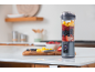 Blender met fruit op aanrecht, met kom frambozen en snijplank op de achtergrond.