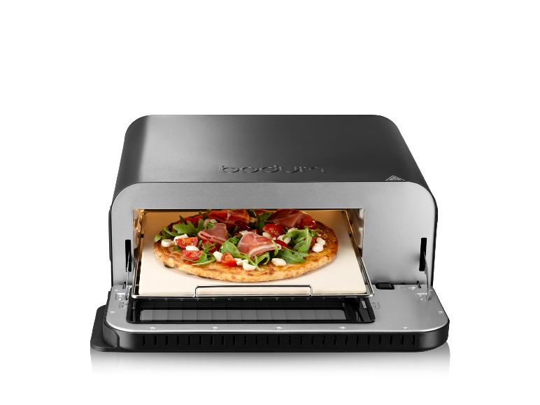 Een Bodum pizzaoven met een pizza met ham, rucola en tomaten erin