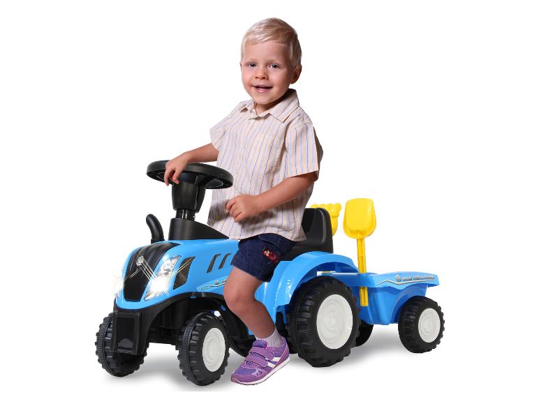 Een peuter zit op een blauwe New Holland speelgoedtractor.