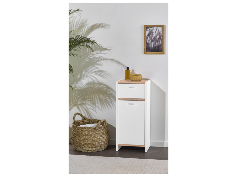 Witte kast met lade en deur, een rieten mand en decoratie.