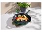 Groene gietijzeren pan met zalm, groenten en kruiden op een houten plank.