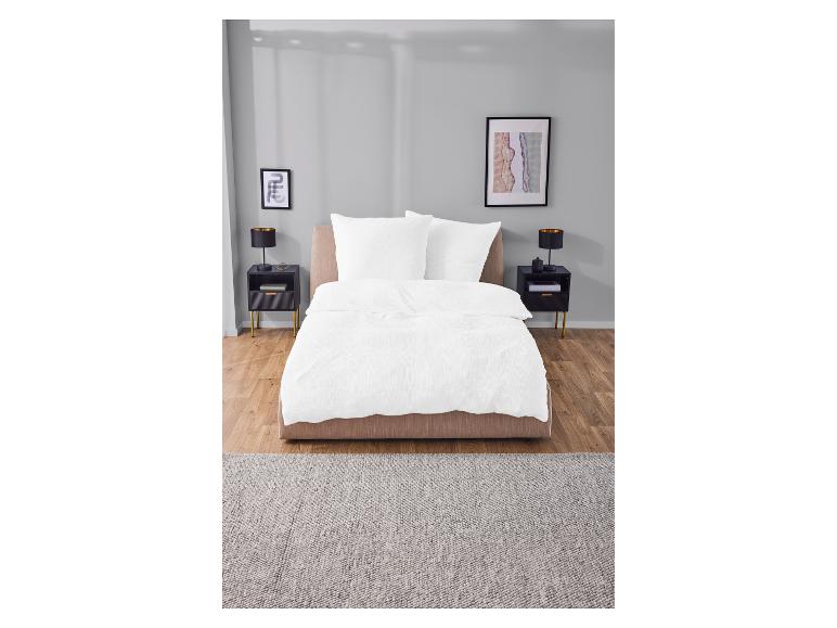 Wit katoenen beddengoed op een beige bed in een moderne slaapkamer.