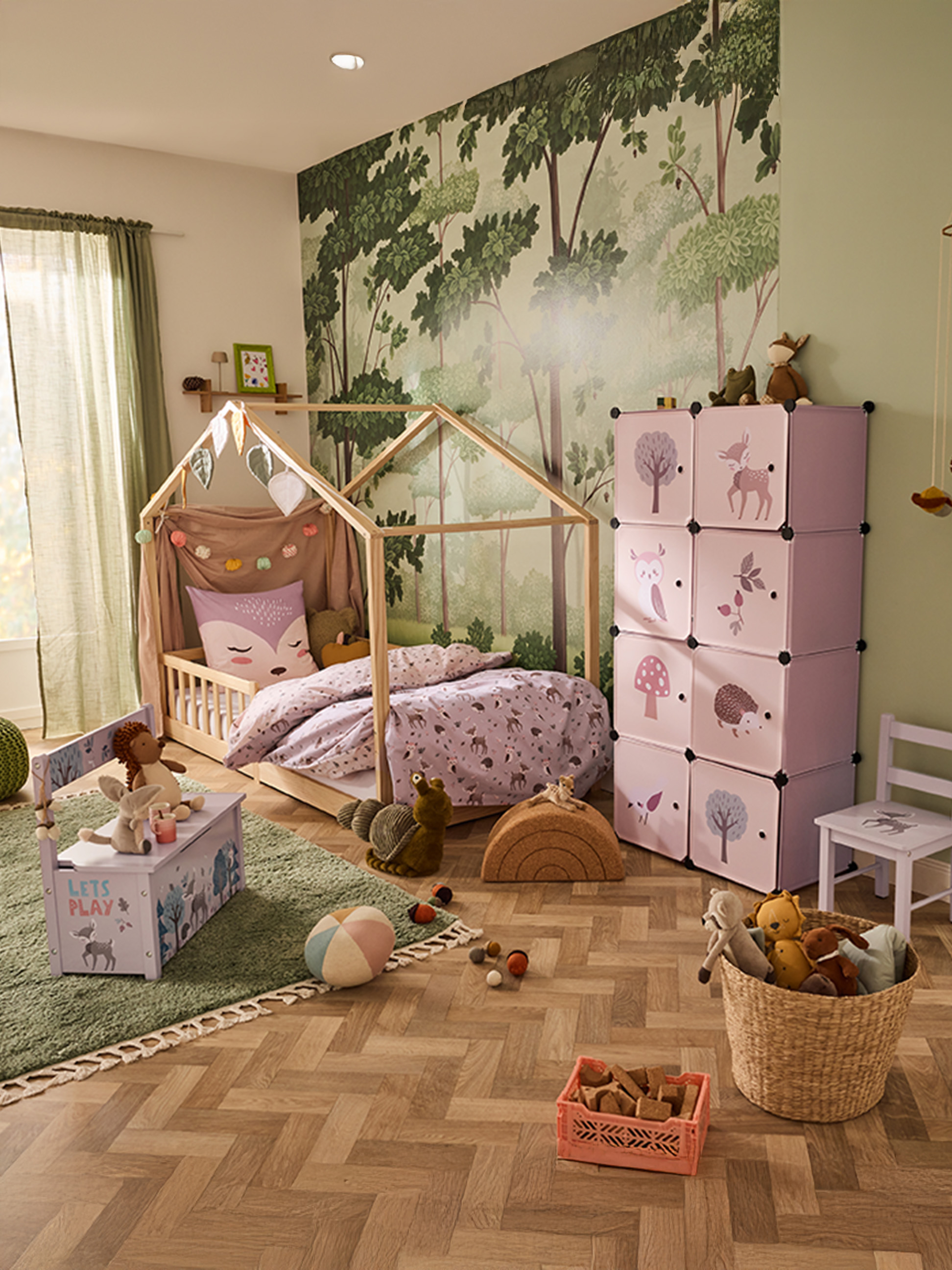 Kinderkamer met huisvormig bed, roze opbergkubussen en bosbehang.