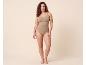 Vrouw in beige corrigerende body, staand tegen een beige achtergrond.