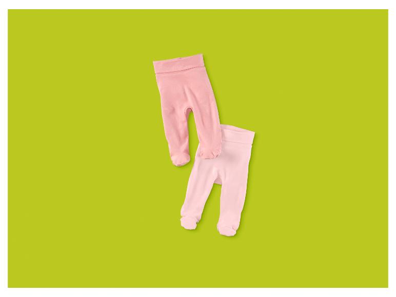 Twee paar roze babybroekjes met voetjes op een groene achtergrond.