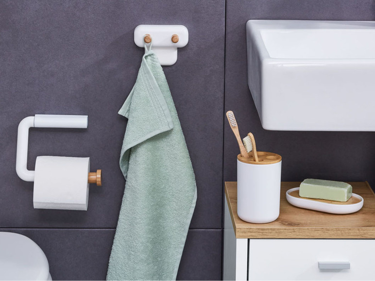 Een badkamer met een handdoek, toiletpapierhouder, tandenborstelhouder en zeepbakje.