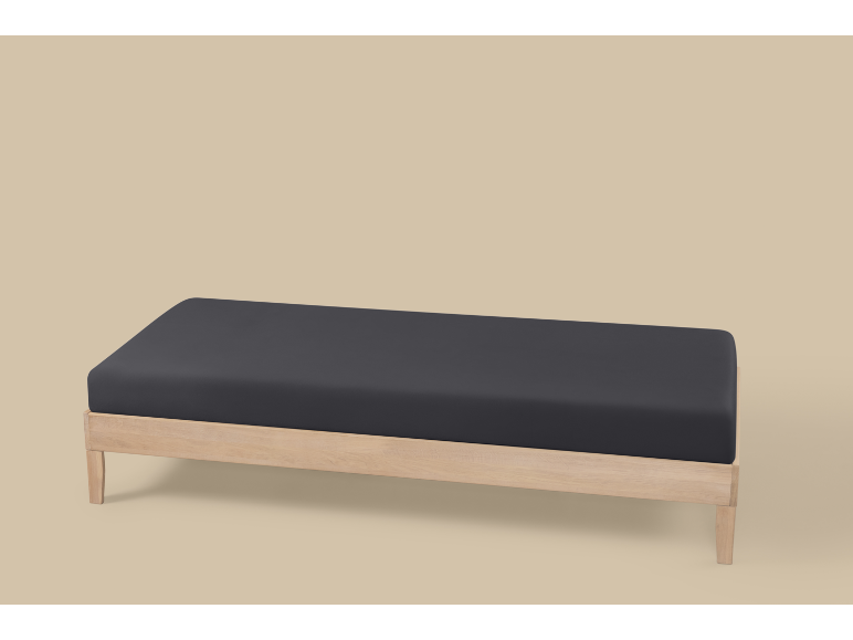 Een houten bedframe met een donkergrijs matras op een lichtbeige achtergrond.