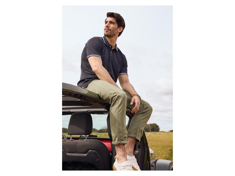 Man in polo shirt en chino's zittend op een Jeep.