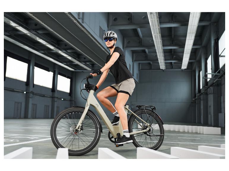 Vrouw met helm en zonnebril rijdt op een elektrische fiets in een binnenruimte.