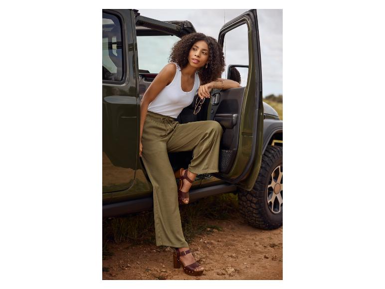 Olijfgroene broek, wit topje en sandalen: stijlvolle vrouw bij een Jeep.