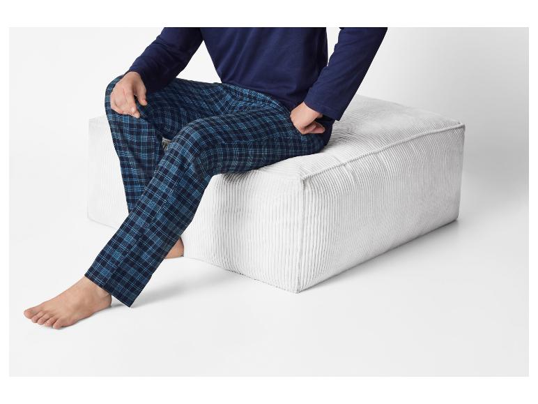 Man in blauw geruite pyjama en marineblauw shirt zittend op een witte poef.